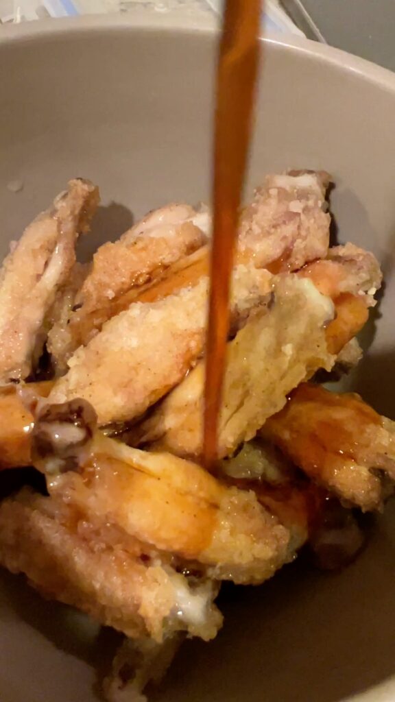 揚げた手羽中に甘辛だれを回しかける様子