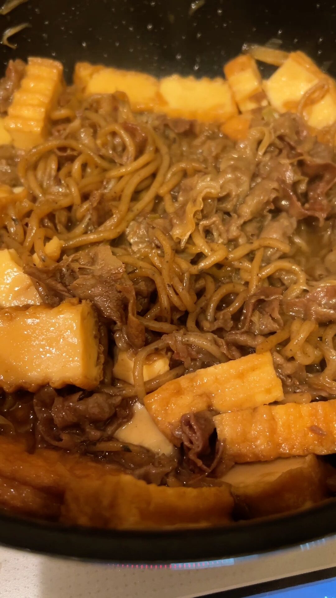 Thinly sliced beef placed on top of shirataki noodles and vegetables in a pan
