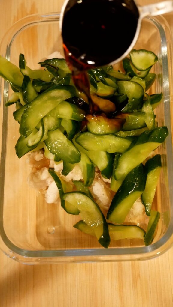 Pouring soy-based dressing over shredded chicken and cucumber