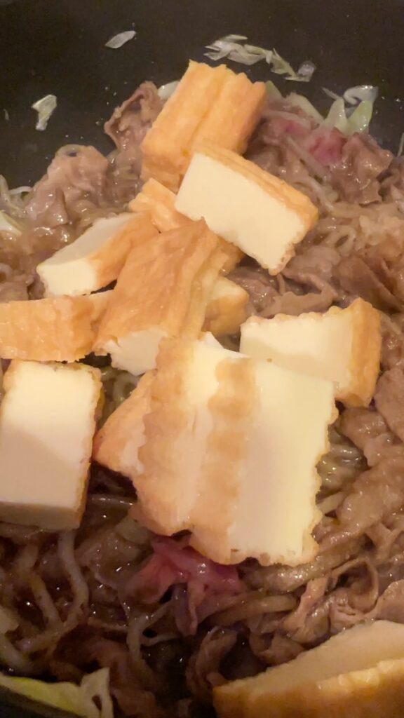 Adding sliced tofu puffs (atsuage) to beef and shirataki in the pan