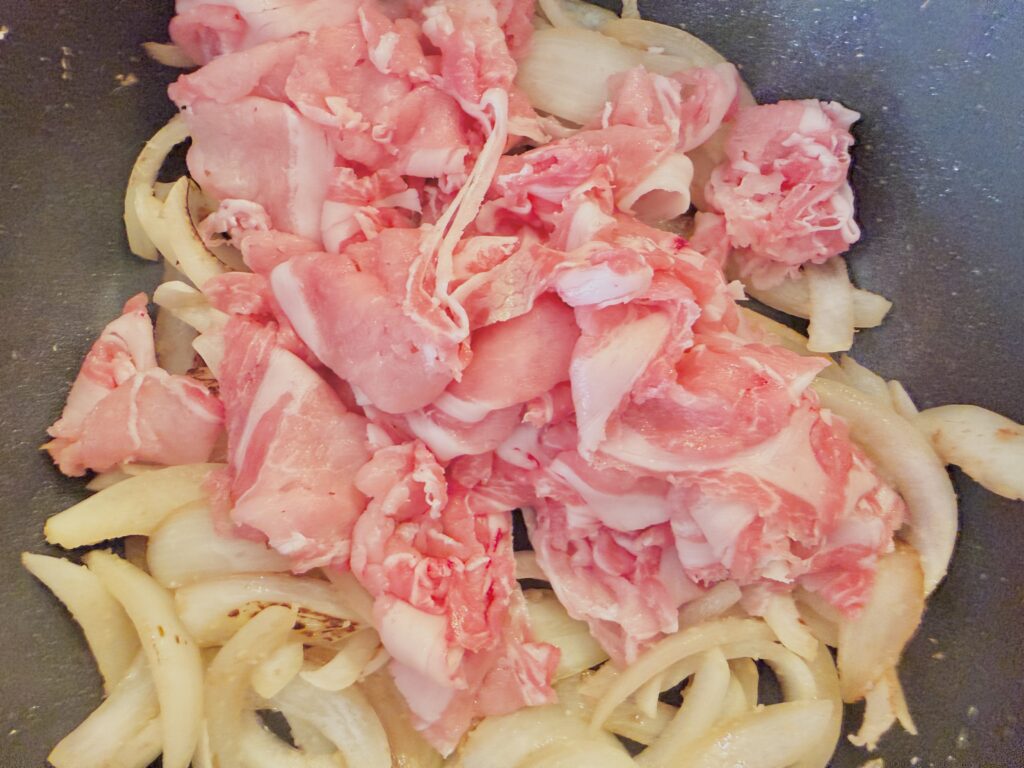 Shogayaki step: add thinly sliced pork to the sautéed onion