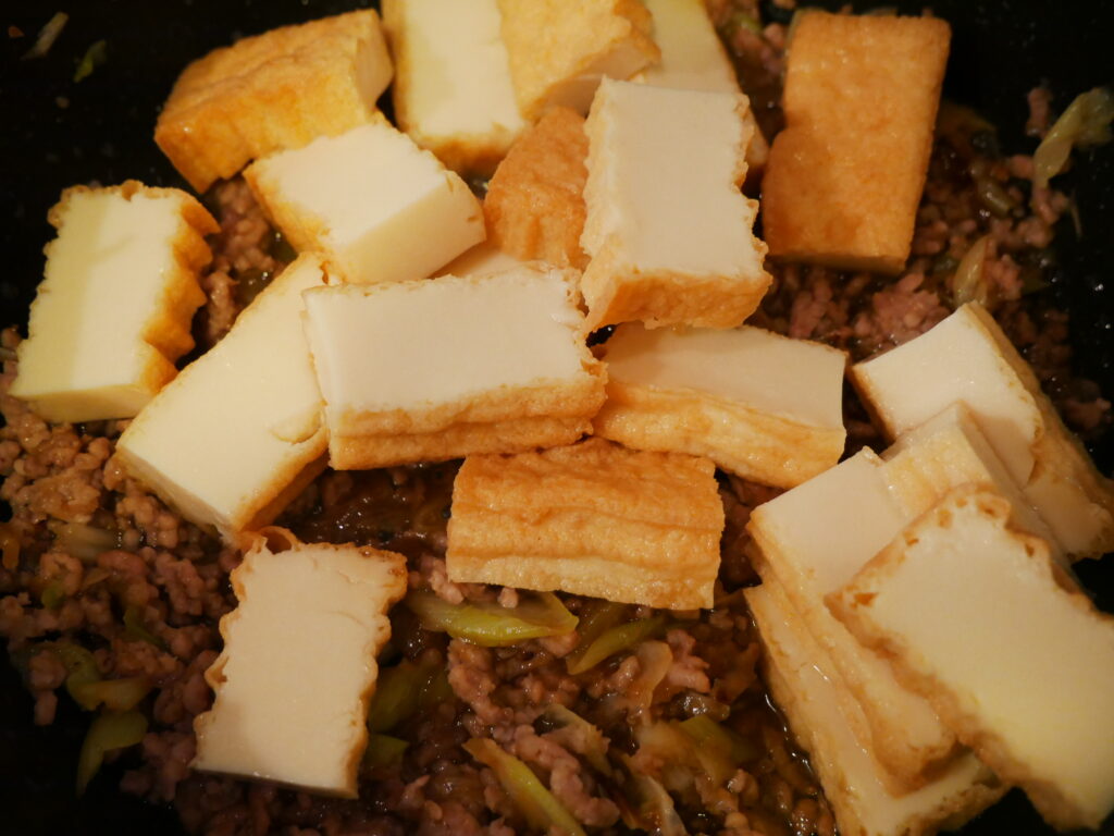 炒めたひき肉の上に食べやすく切った厚揚げを加えた工程写真