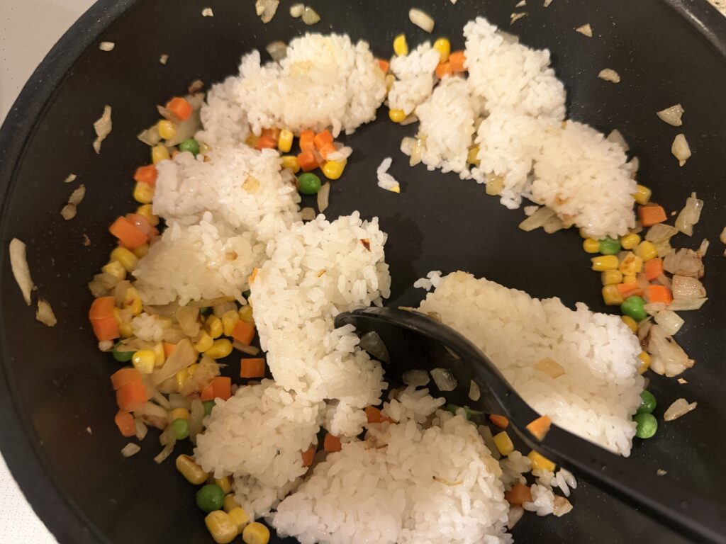 炒めた野菜にごはんを加えて混ぜ始めている様子