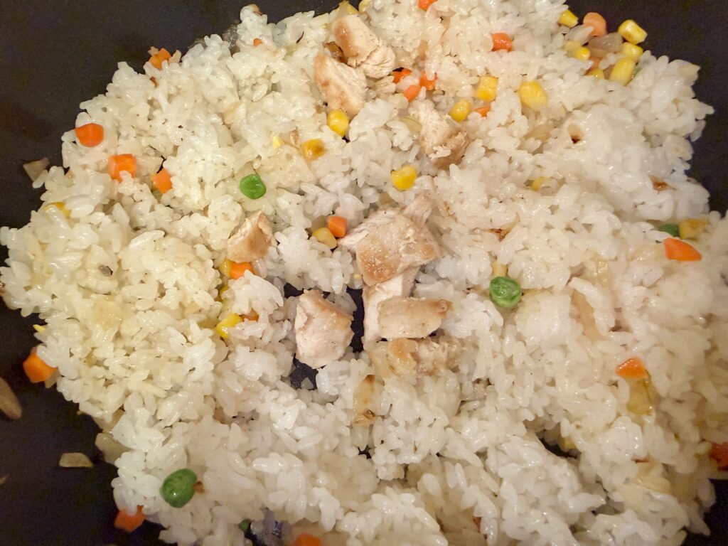 三色ピラフに焼いた鶏むね肉を加え、塩を振って仕上げる様子