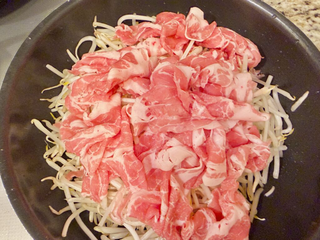 もやしの上に豚こま肉を重ねて並べた簡単調理の工程写真