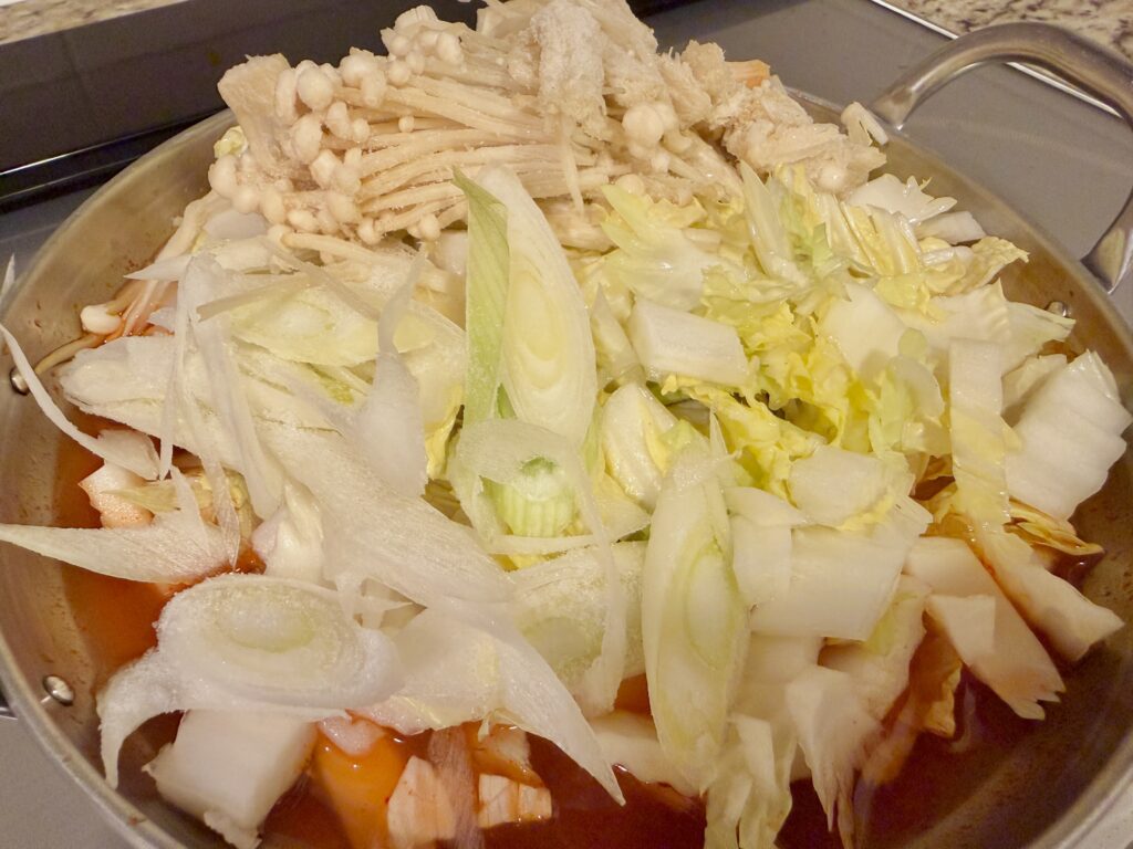 久原 あごだし旨辛鍋に白菜・長ねぎ・えのき・豚肉を入れた状態