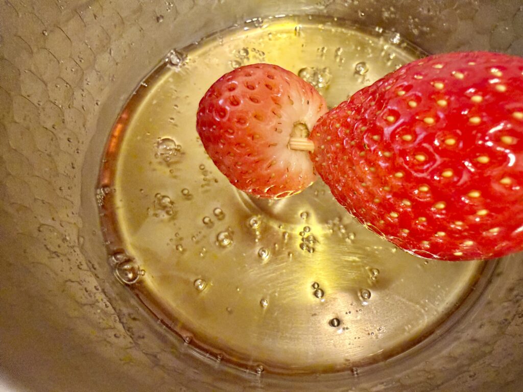 いちごを飴にくぐらせてコーティングする工程