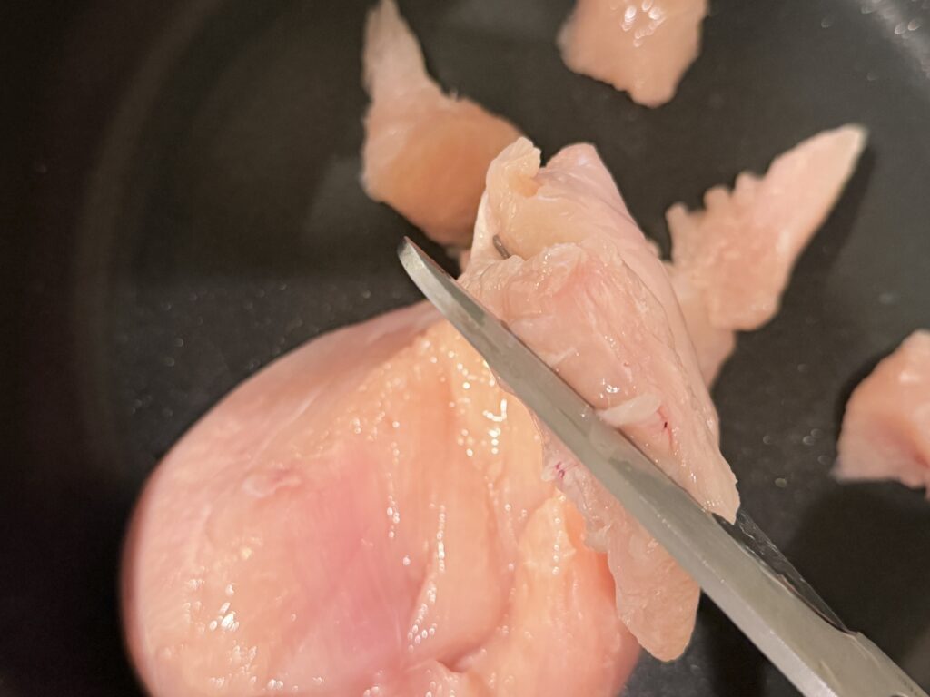 コストコさくら鶏胸肉をキッチンバサミでフライパンに直接カットしている様子
