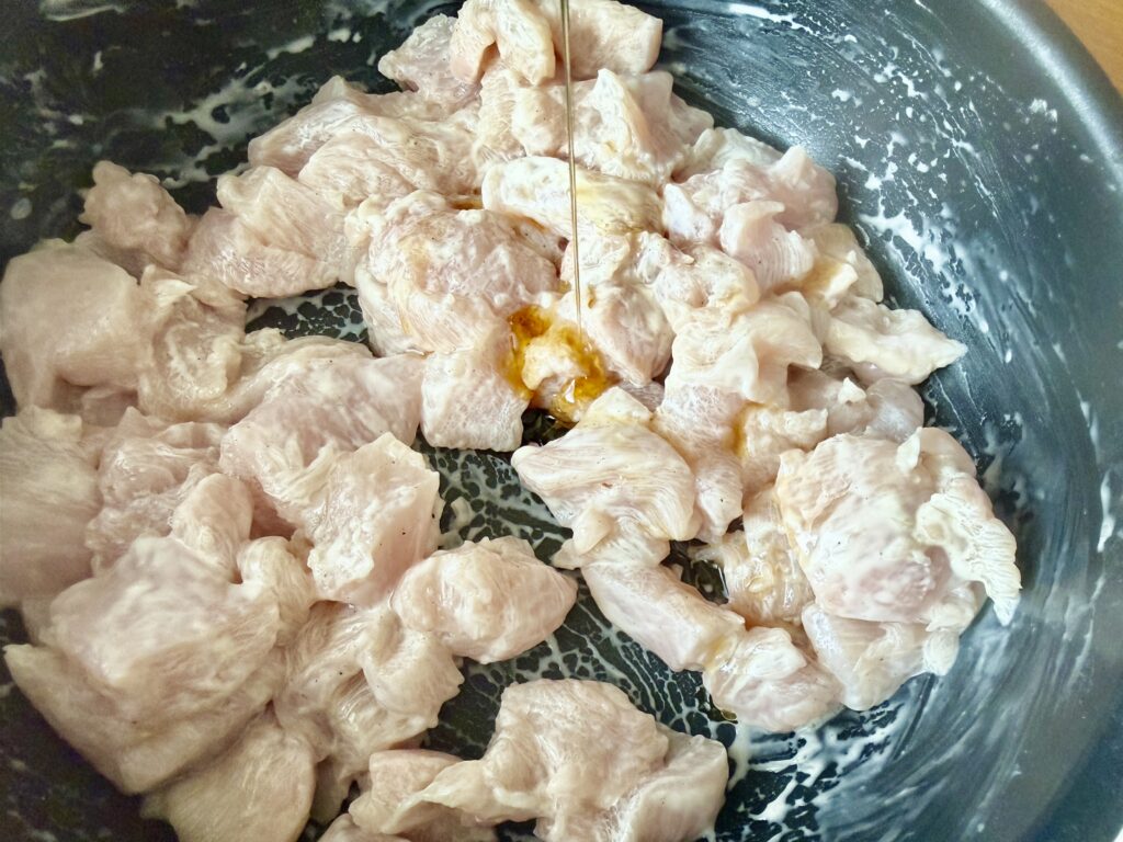 下味をつけた鶏胸肉にごま油を回しかけている様子