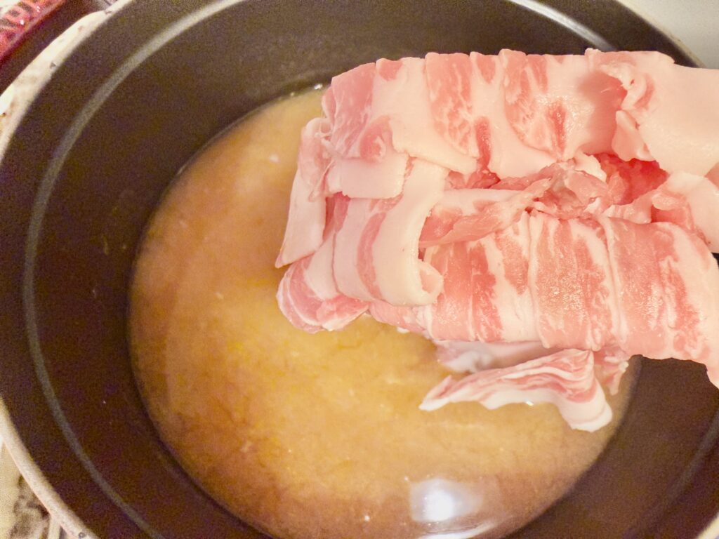味噌だしに豚バラ肉を加える様子