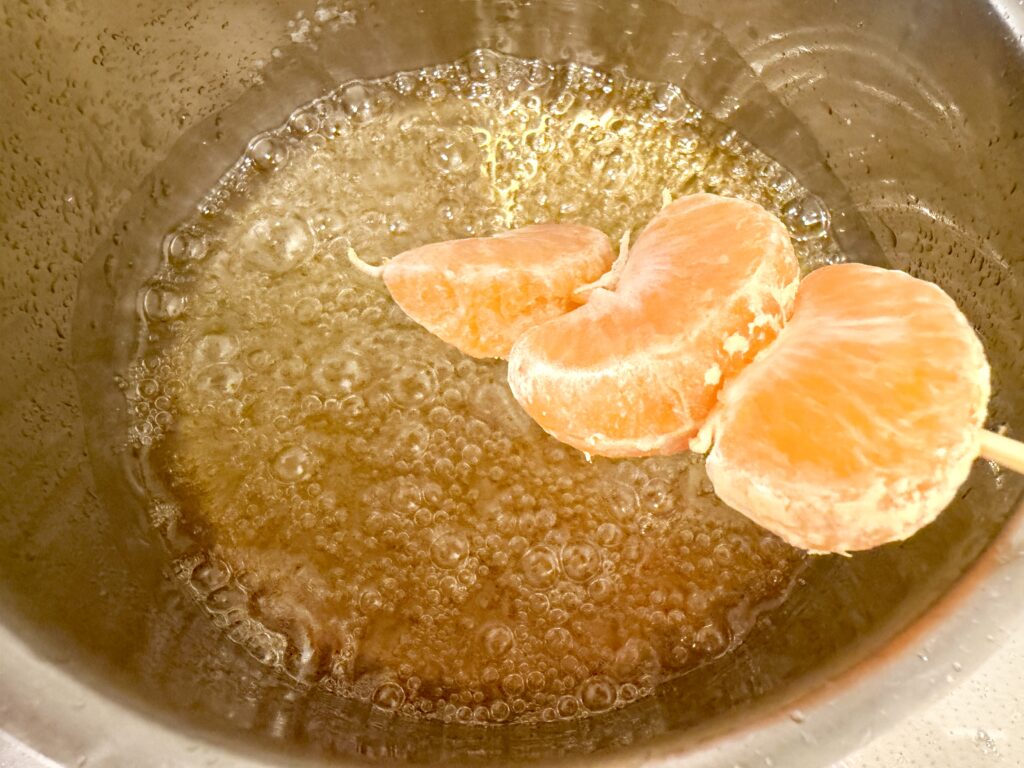 みかんを飴にくぐらせてコーティングする様子