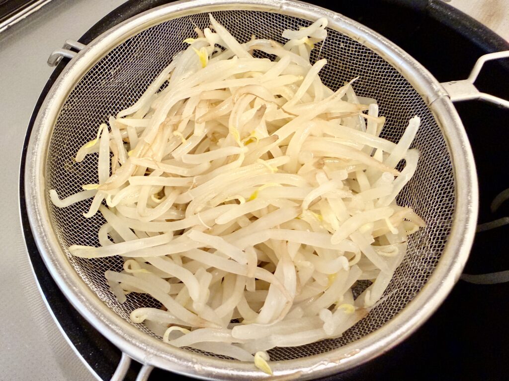 茹でたもやしをざるにあげて水気を切る