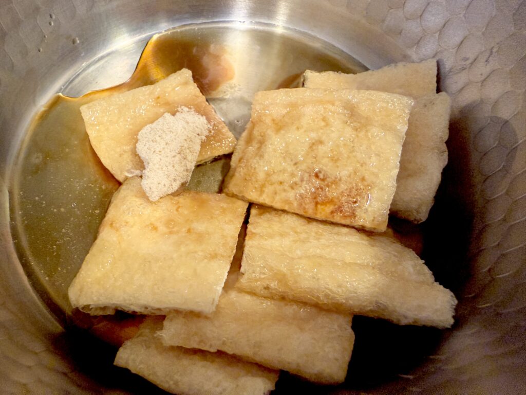 いなり寿司用油揚げに醤油やだしを加えて煮る様子