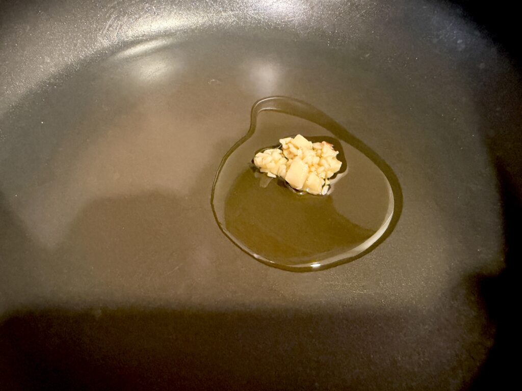 ケール炒めを作るためにごま油と刻みにんにくをフライパンで熱している様子