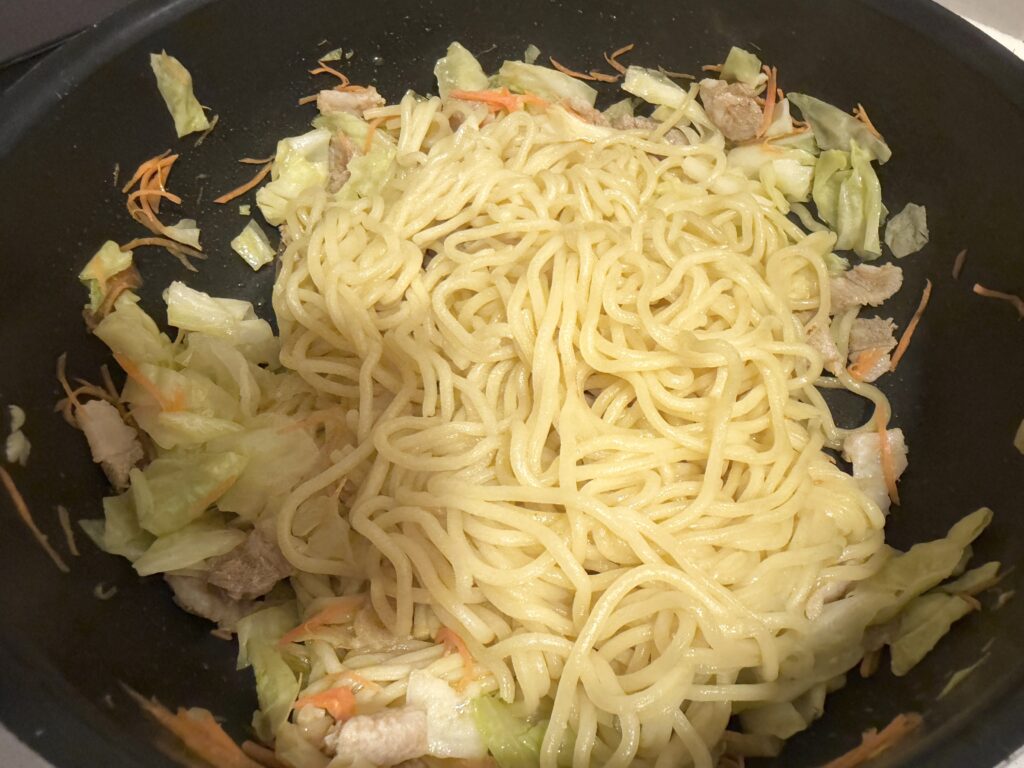 野菜と豚肉を炒めたフライパンに焼きそば麺を加える