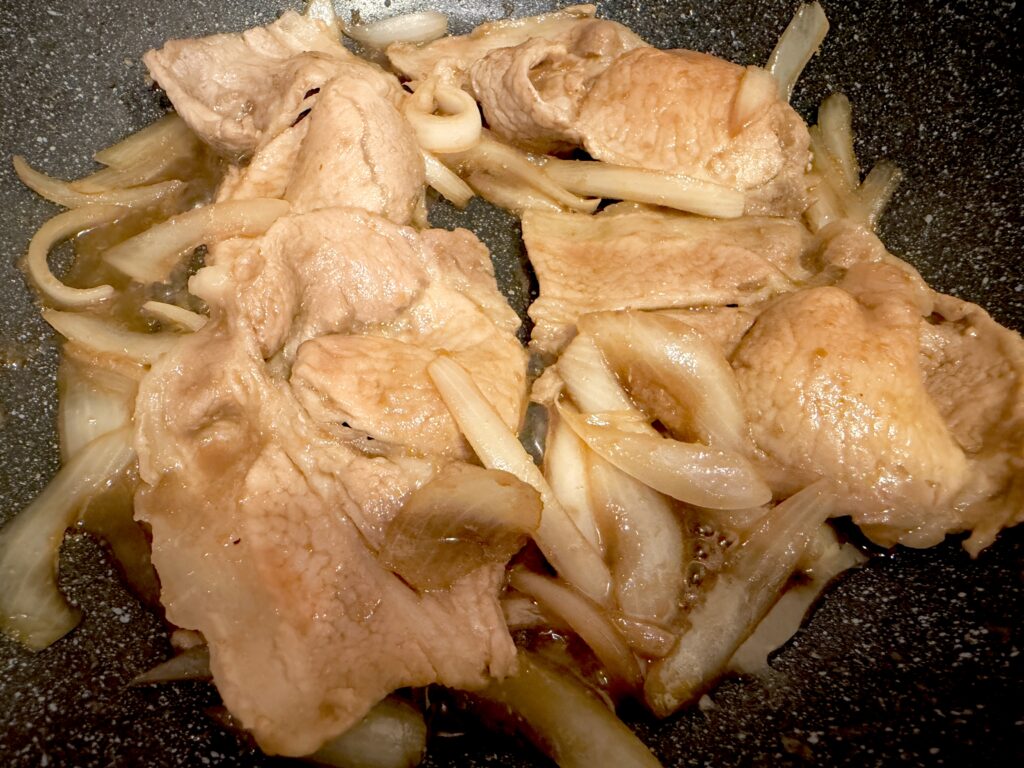 豚肉と玉ねぎへ生姜焼きのタレを煮絡めている様子
