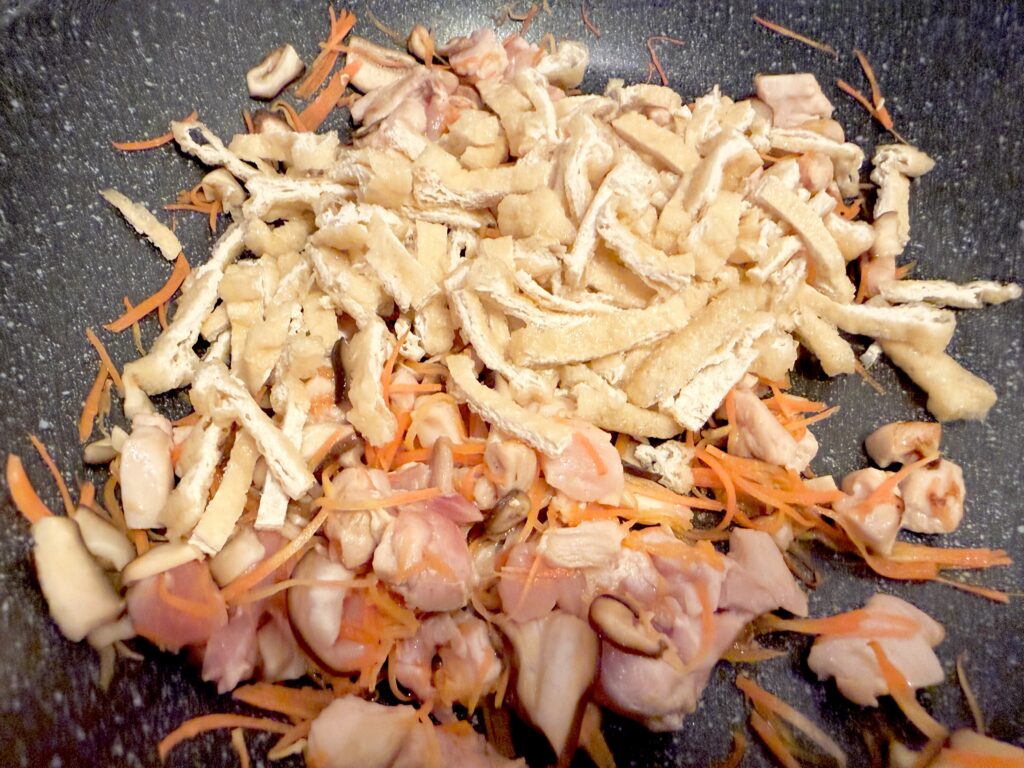 炒めた鶏肉と野菜に細切りの油揚げを加える様子