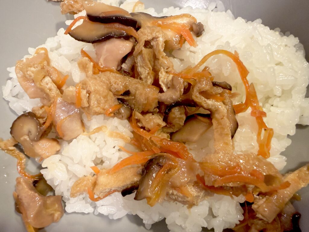 温かい白ご飯に鶏肉と油揚げの甘辛い具を加える様子