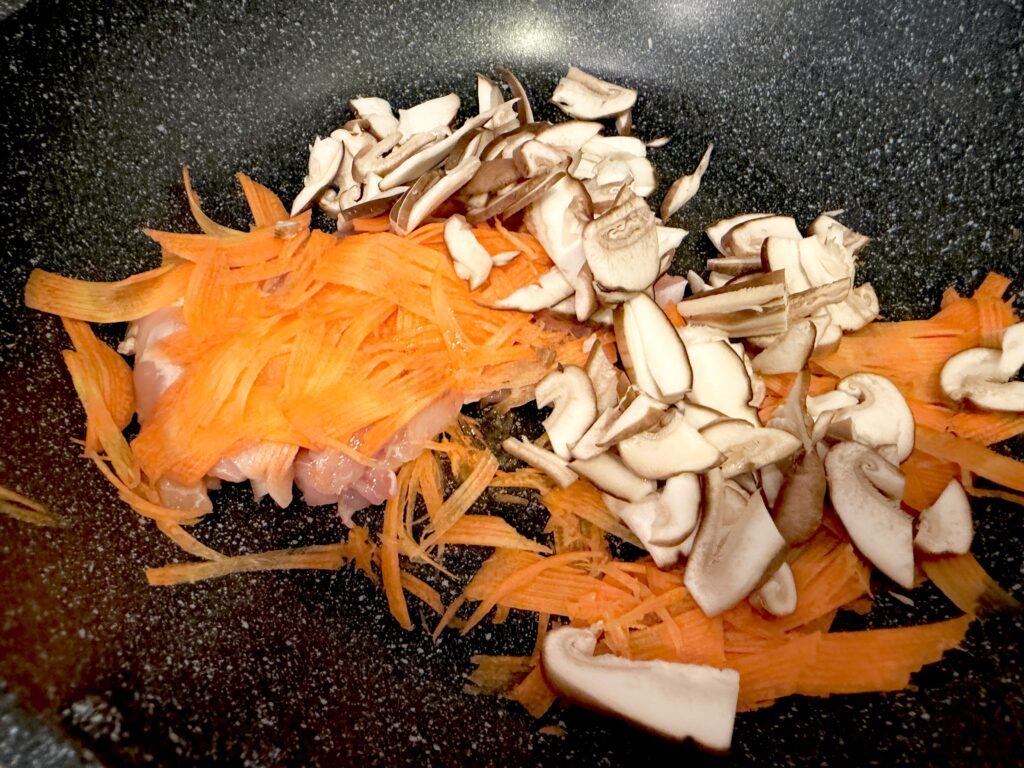 鶏肉とにんじんを炒めたフライパンへしいたけを加える様子