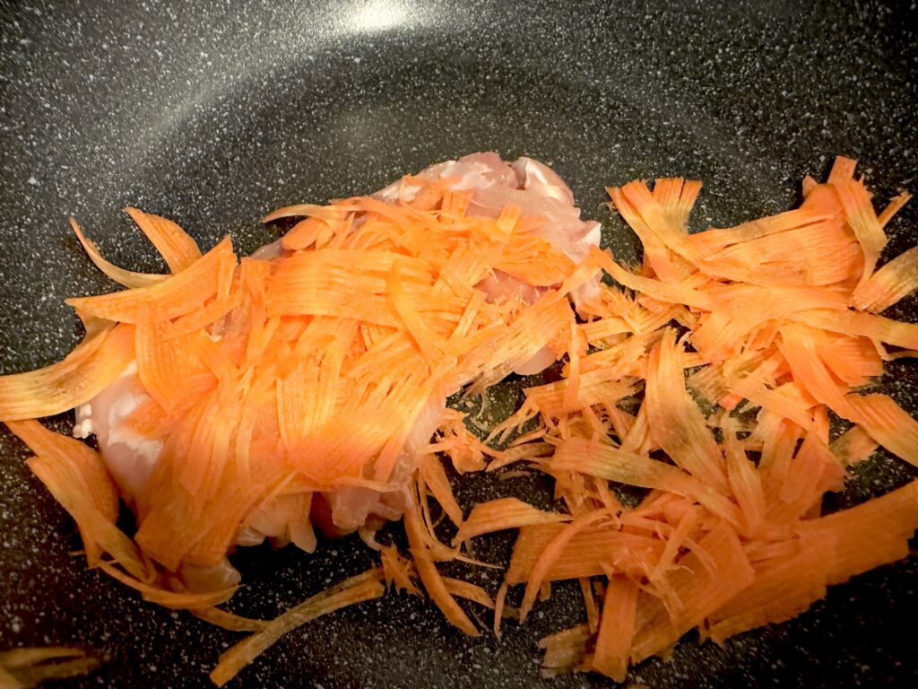 フライパンで鶏肉と細切りにんじんを炒める様子