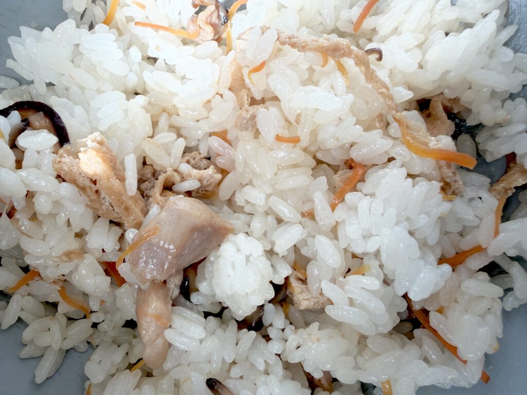 炊きたての白ご飯と鶏肉・にんじん・しいたけ・油揚げを混ぜる様子